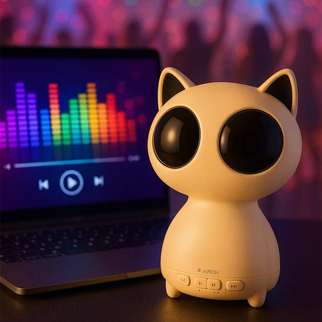 A cute, cat-shaped portable speaker with large black eyes sits on a dark tabletop in front of a laptop showing a colorful audio equalizer screen. The background is a soft, out-of-focus purple and pink bokeh with silhouettes of people, suggesting a party or concert atmosphere.